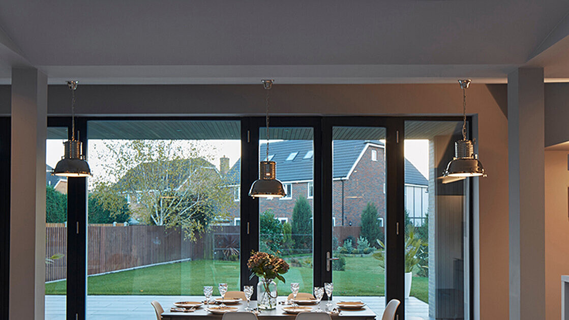 Moderner Essbereich mit Blick durch große Glasfront auf Garten im Abendlicht.