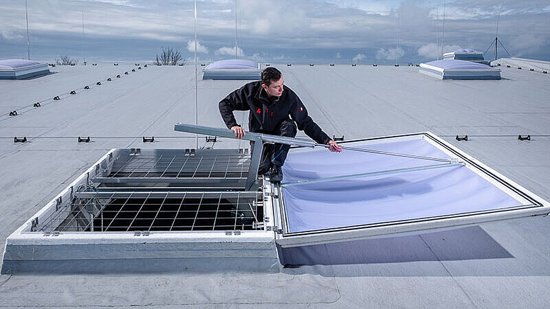 Monteur bei der Wartung einer Lichtkuppel auf einer Produktionshalle.