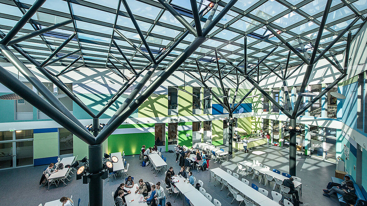 Une construction en acier symbolise des arbres sous un toit en verre Construction en acier et verre au-dessus de la salle de classe de l'IS Bonn | insights by LAMILUX