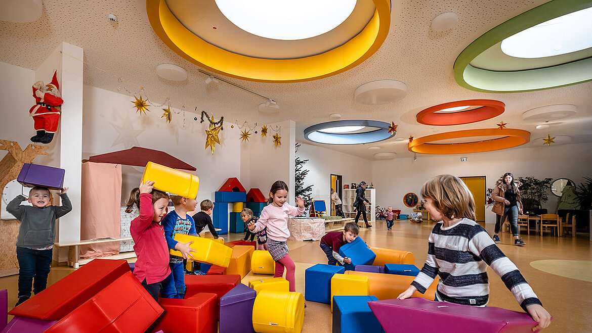 Les enfants de la crèche jouent sous des éléments colorés laissant passer la lumière du jour